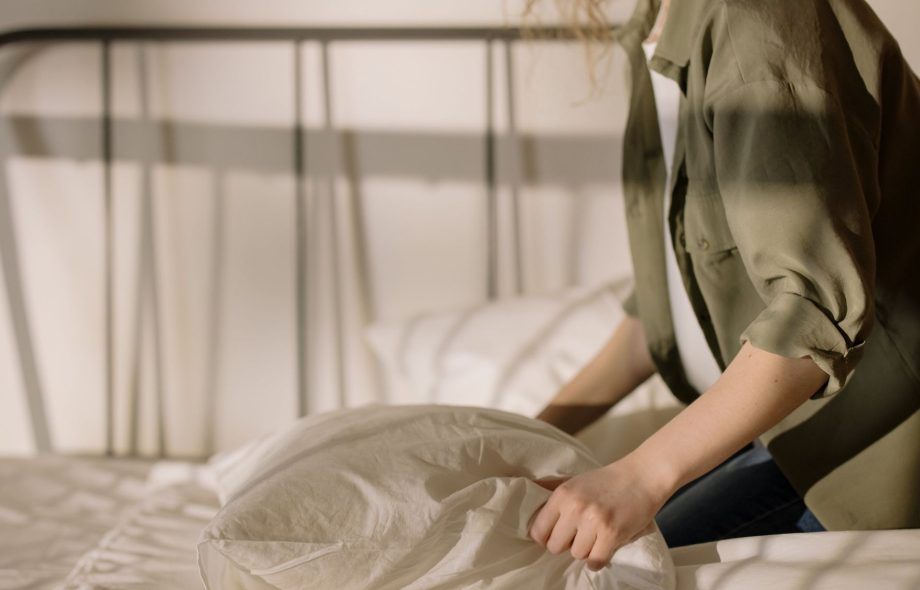 A woman wearing an olive green linen shirt, setting the linen bed sheets