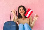 Young woman with suitcase holding Austrian flag symbolizing study abroad opportunities in Austria.
