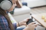 Girl wearing headphones playing a mobile game, representing immersive adaptive game audio technology.